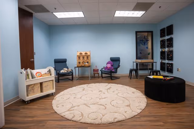 Bright interior room with blue walls, circular rug, chairs, and toys.