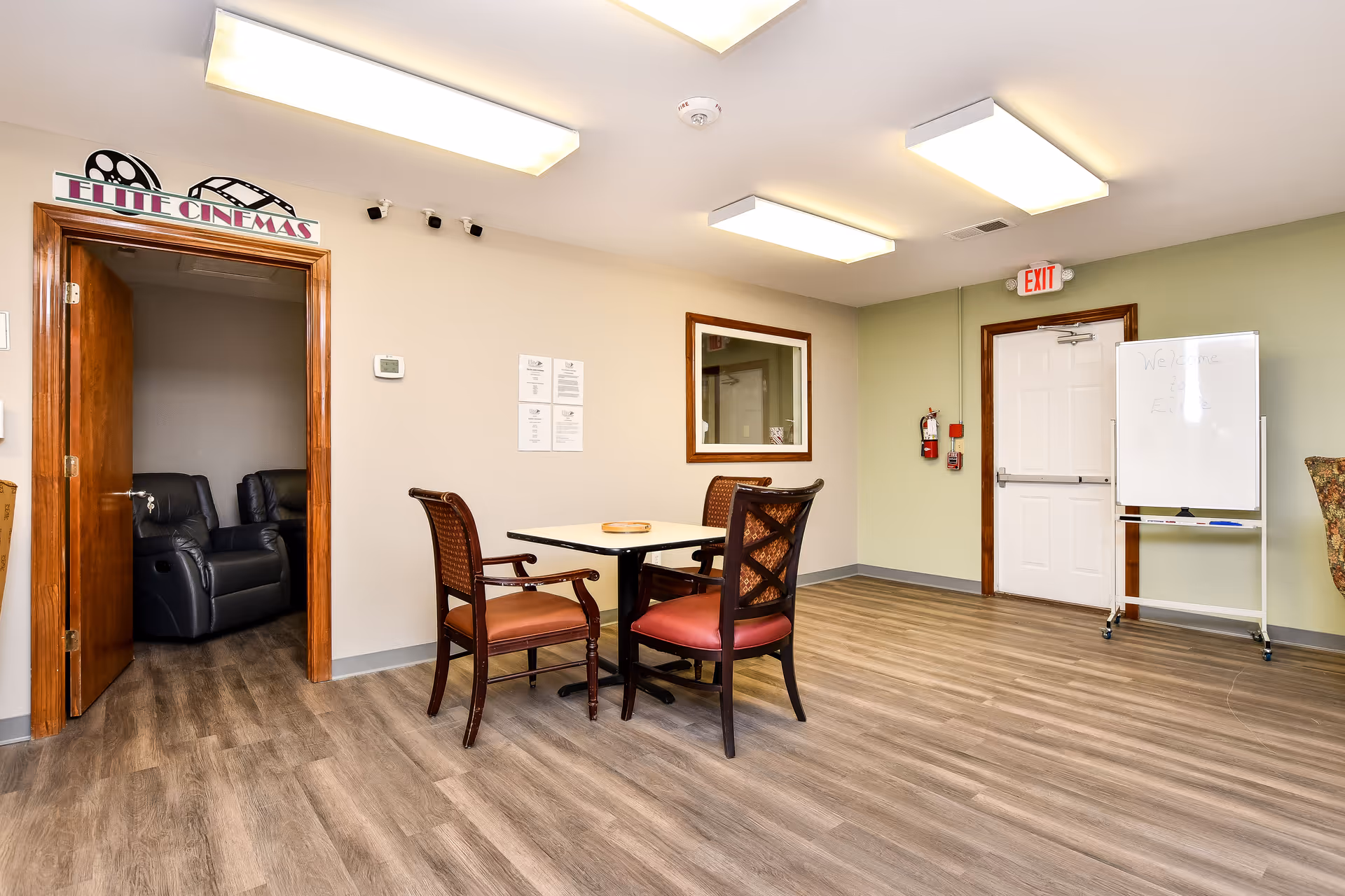 Spacious indoor lounge with a table, chairs, Elite Cinemas entrance, and whiteboard.
