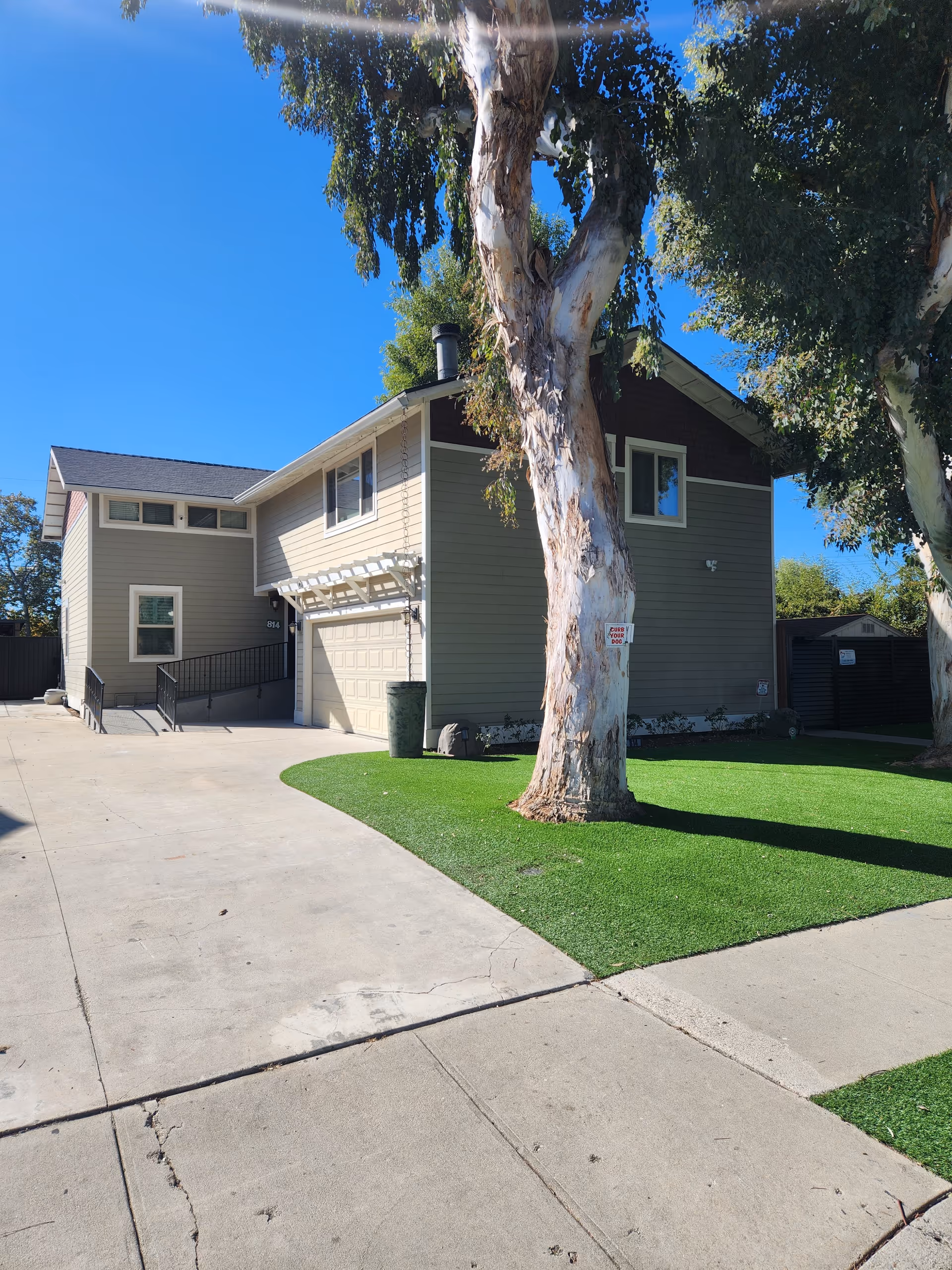 Two-story beige senior living building with driveway and green lawn beneath a clear blue sky.