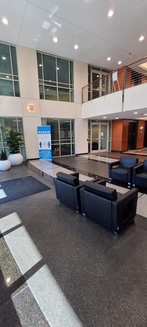 Modern senior living lobby with black seating, large windows, and a mezzanine balcony.
