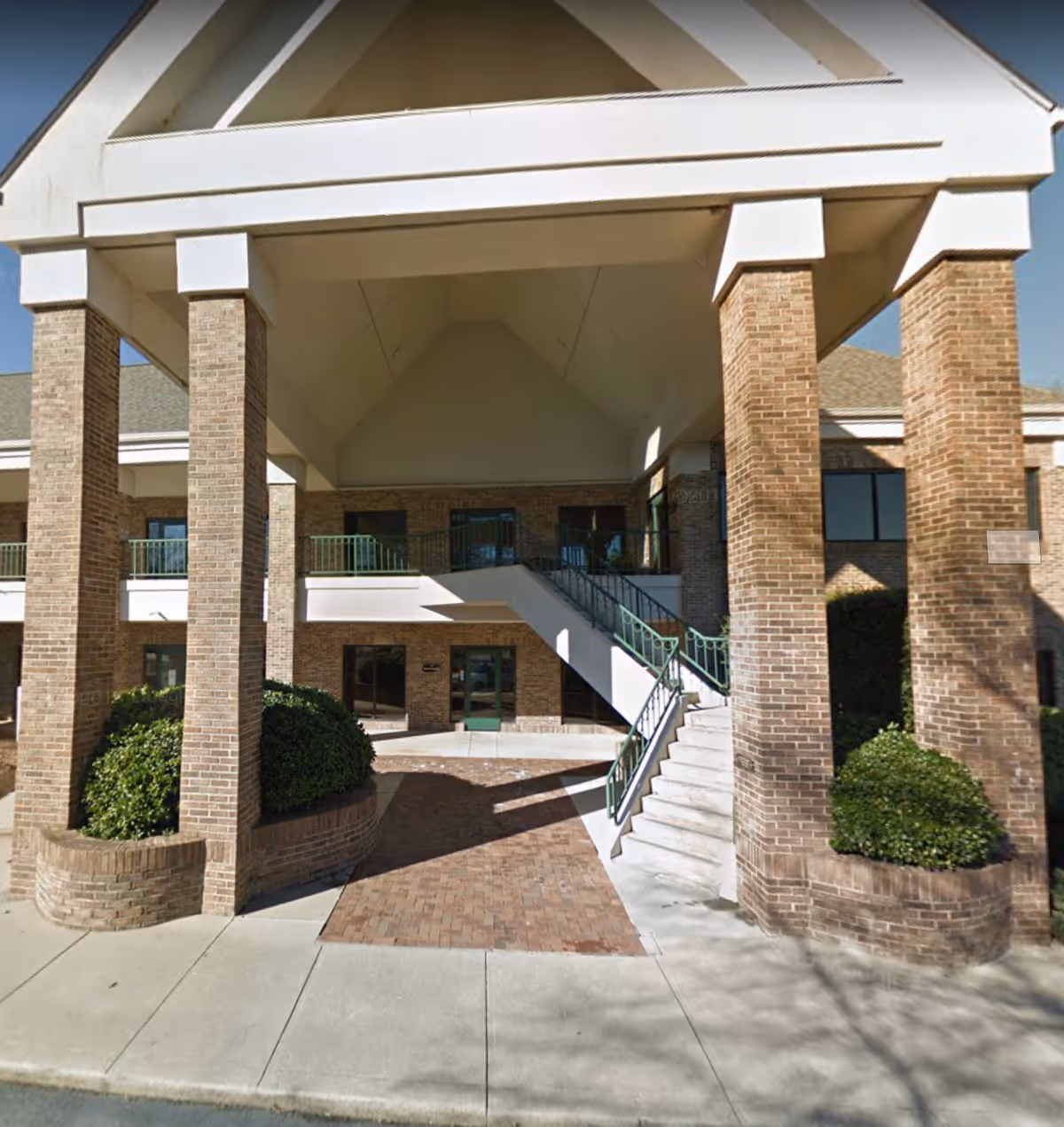 Brick building entrance with tall pillars, stairs, and a covered entrance canopy.