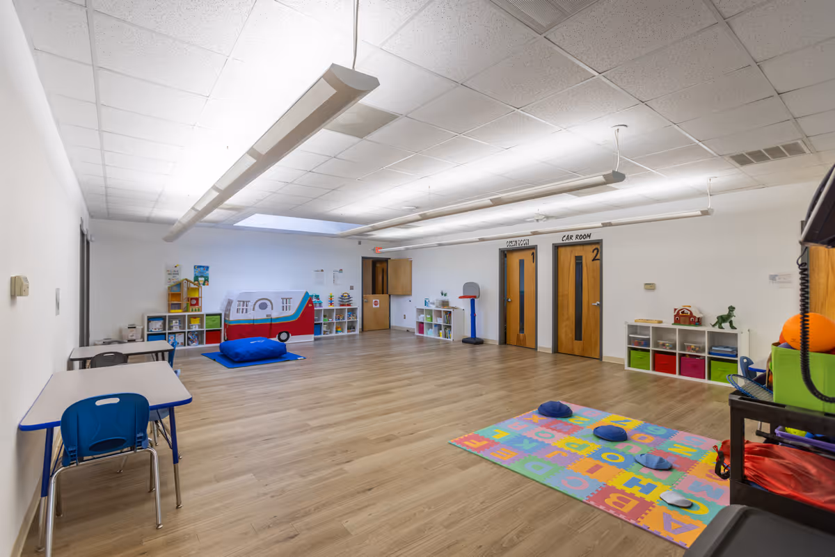 Spacious indoor playroom with toys, mats, and shelves in a senior care facility.