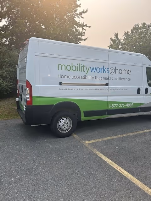 A MobilityWorks van with green branding parked in a lot with trees behind.
