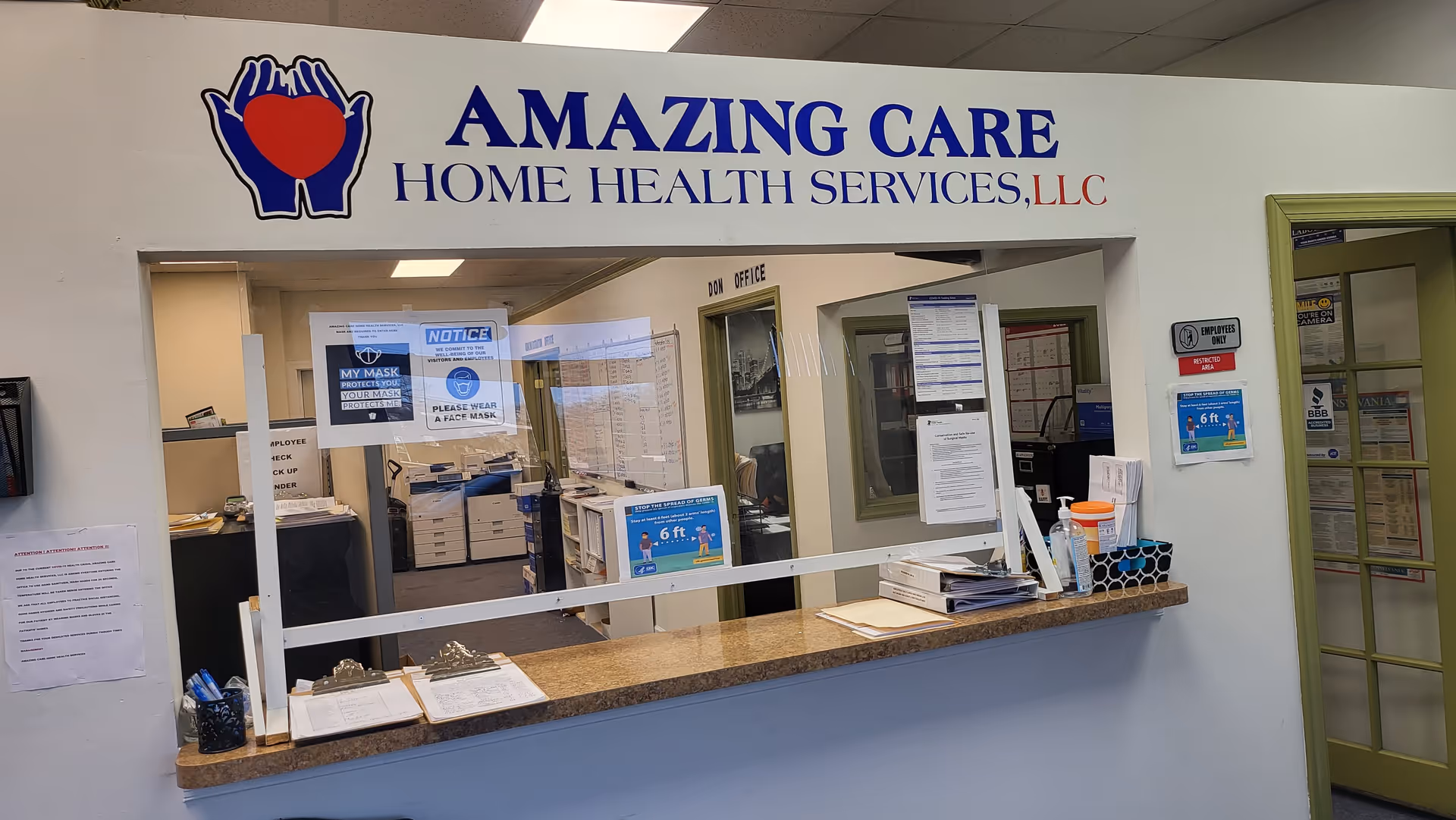 Reception counter inside Amazing Care Home Health Services with notices, paperwork, and glass partition.