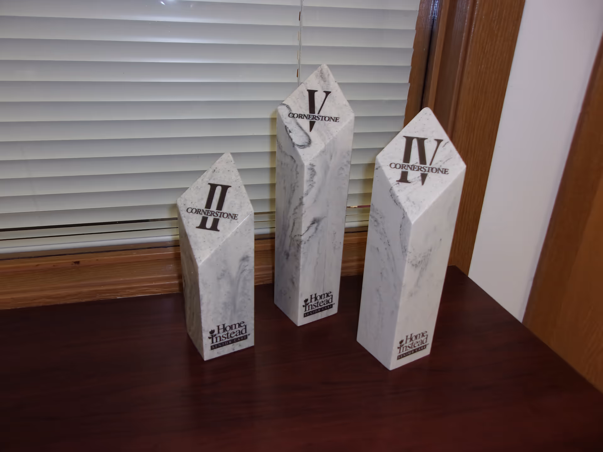 Three marble obelisk decorations with Cornerstone and Home Instead logos sit on a dark wooden table.