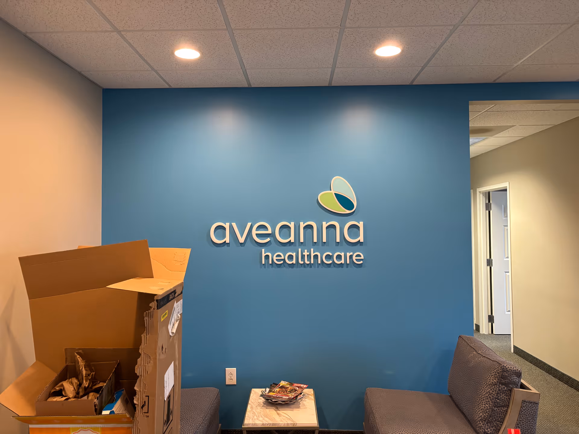 Blue wall with Aveanna Healthcare logo in a small lobby with seating and boxes.
