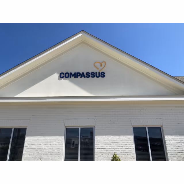 White brick building with Compassus sign and triangular roof against blue sky