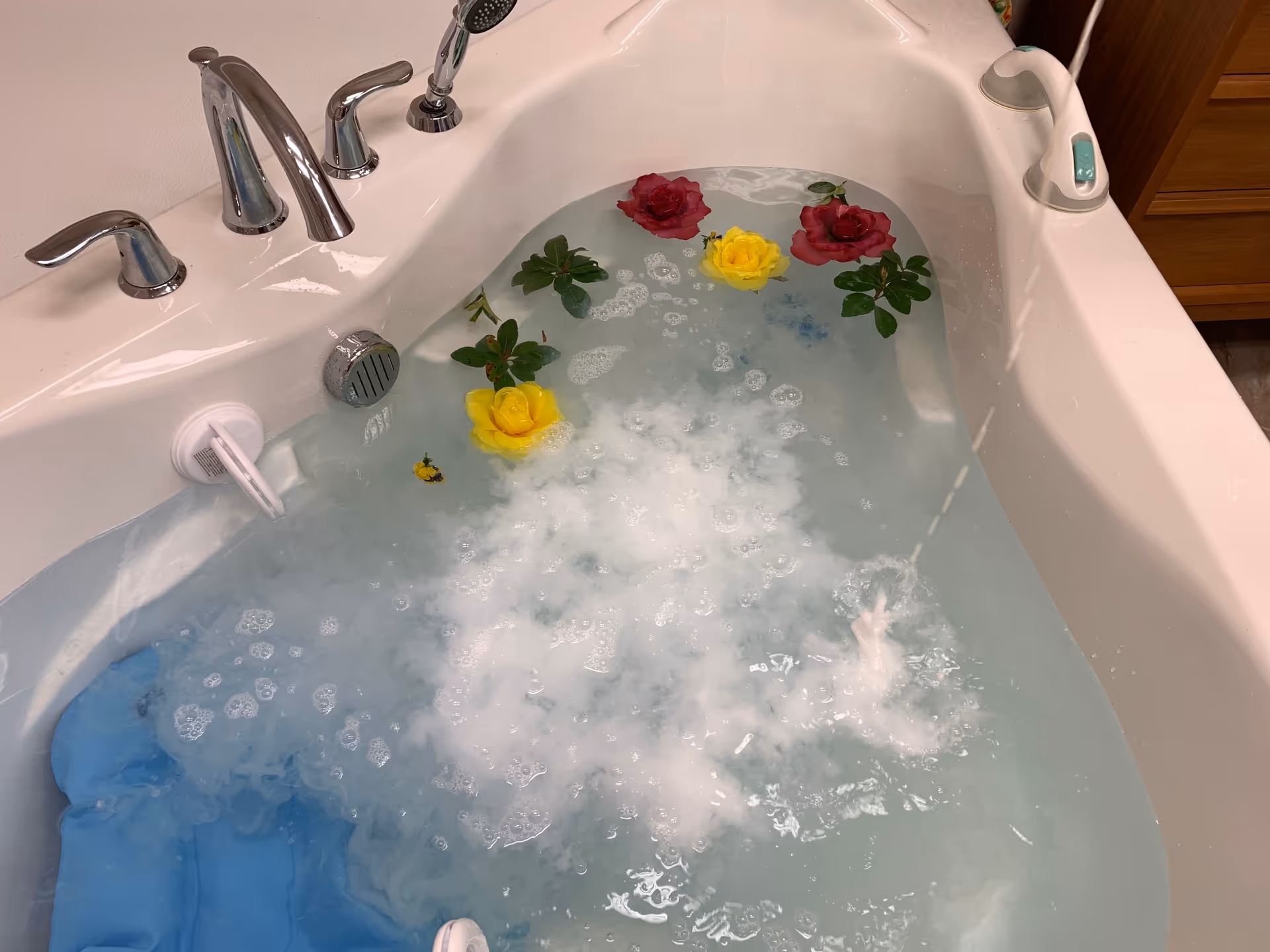 White bathtub filled with bubbly water and floating yellow and red roses.