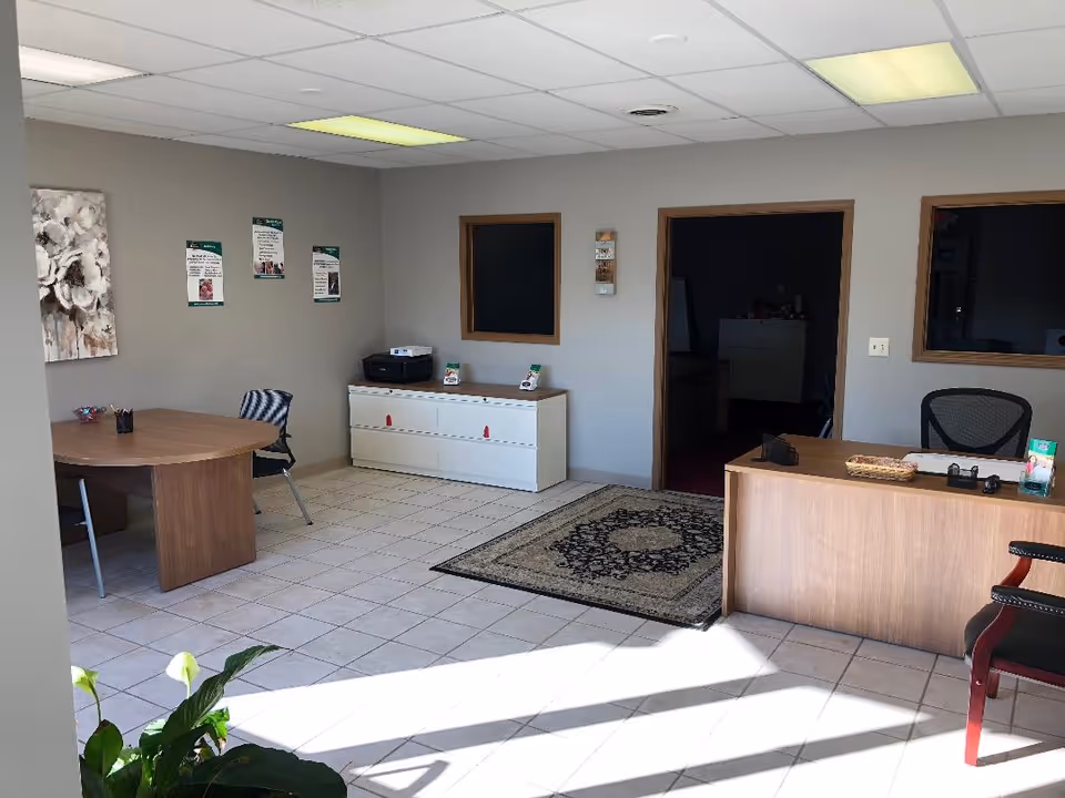 Interior reception area with desk, round table, cabinets, rug, and posters.