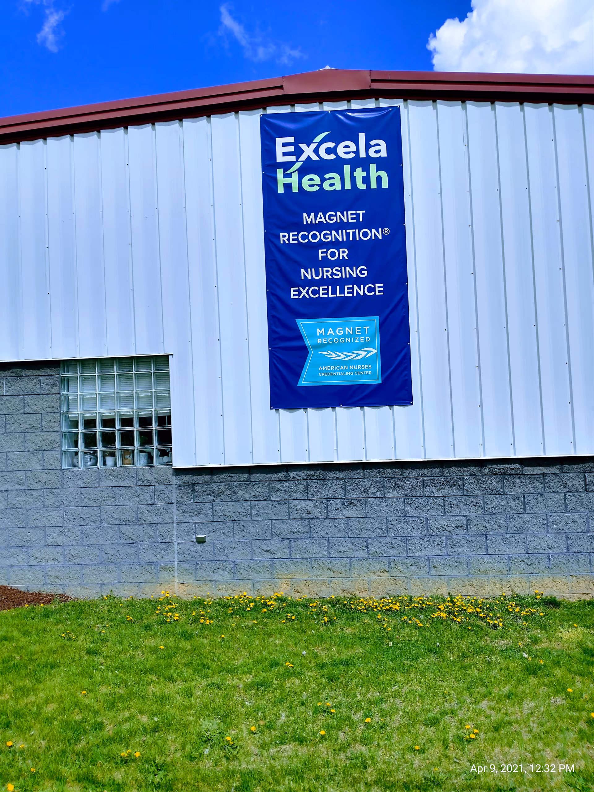 Blue Excela Health banner on a gray building exterior with a glass-block window.