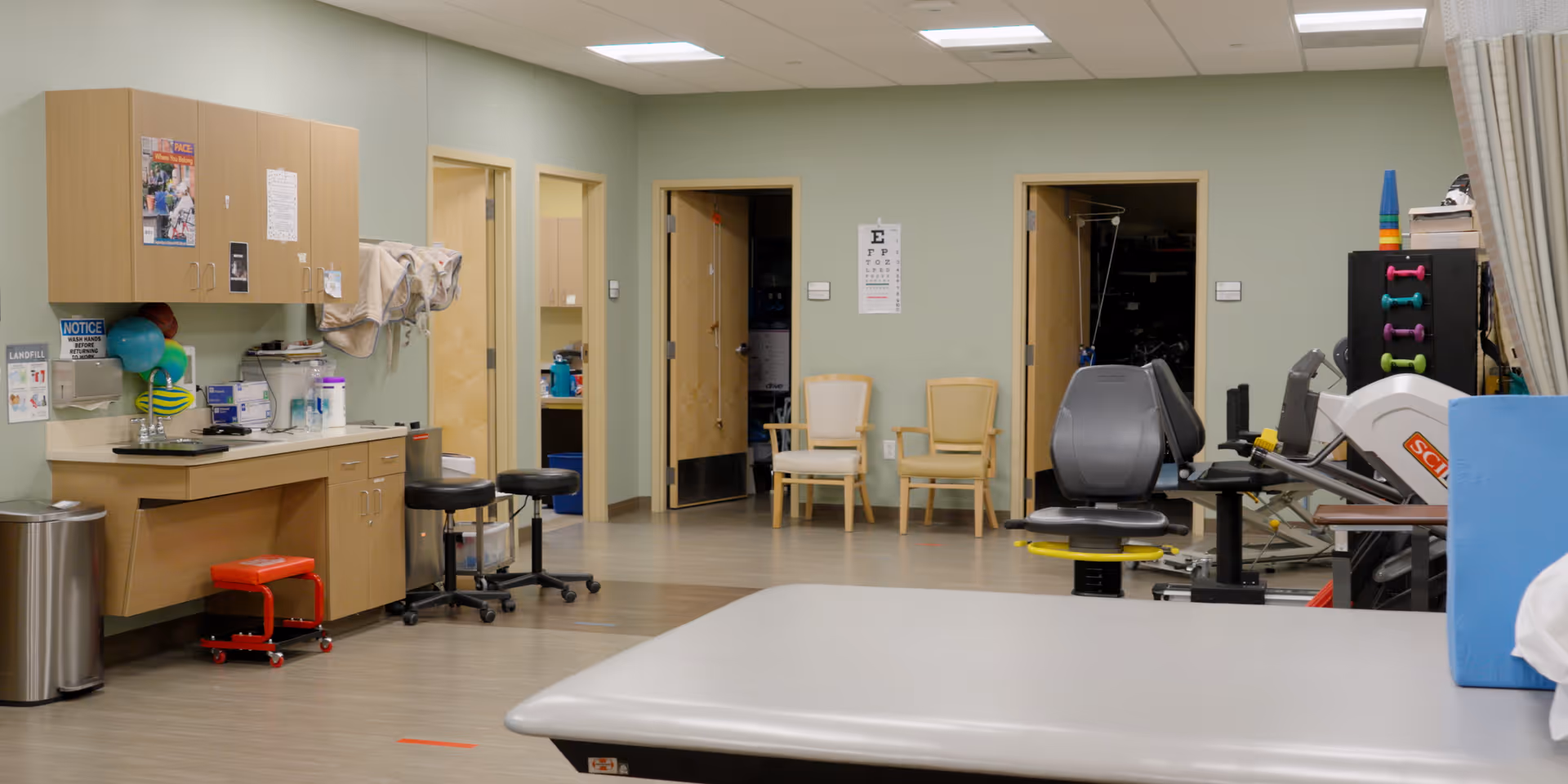 Interior therapy and rehabilitation room with cabinets, chairs, and exercise equipment.