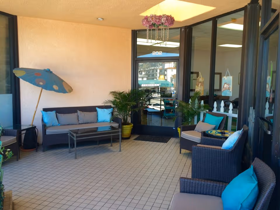 Outdoor lounge area with wicker seating, turquoise cushions, plants, and glass doors.