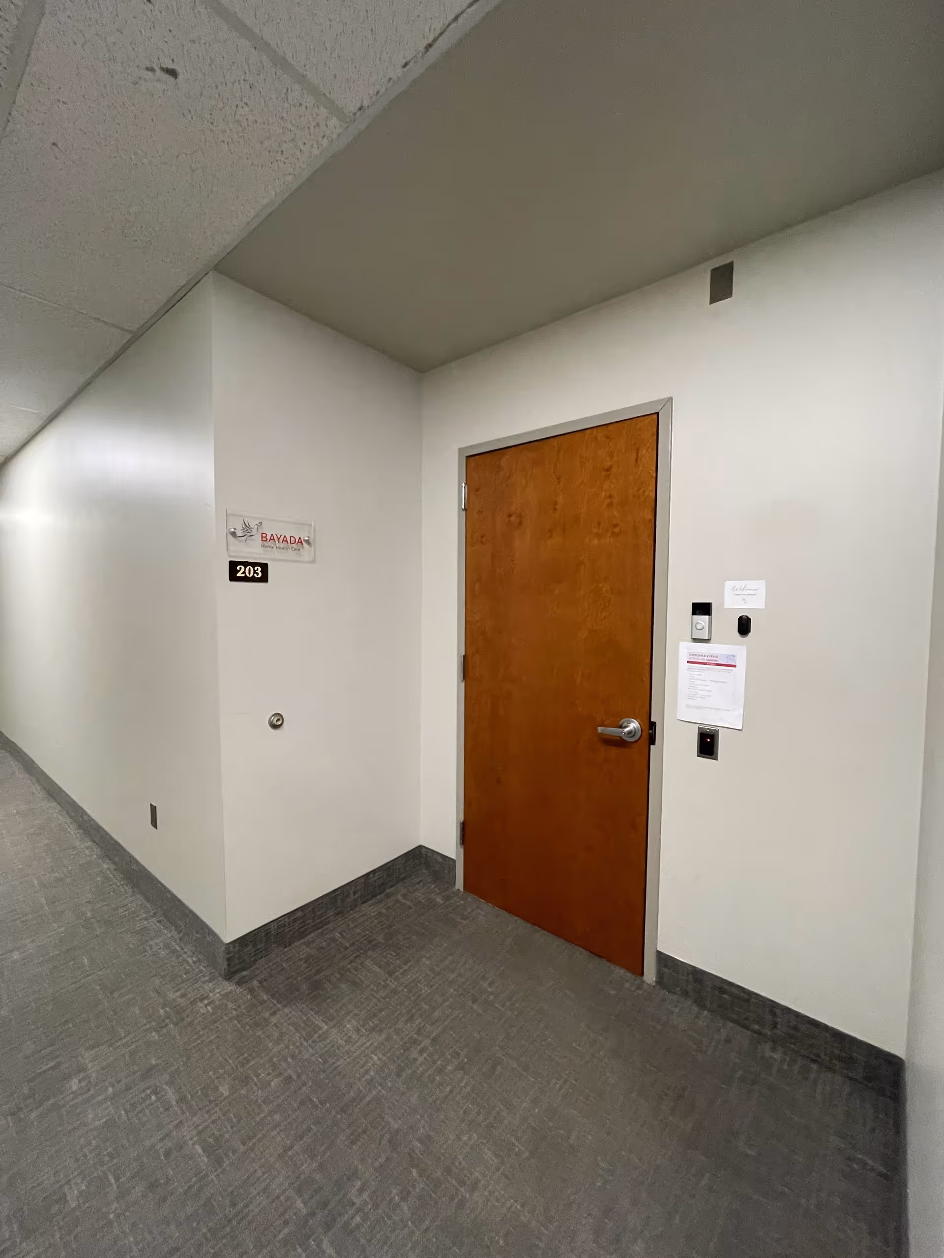 Interior hallway with a wooden door, wall sign, and room number 203 in a Bayada facility.