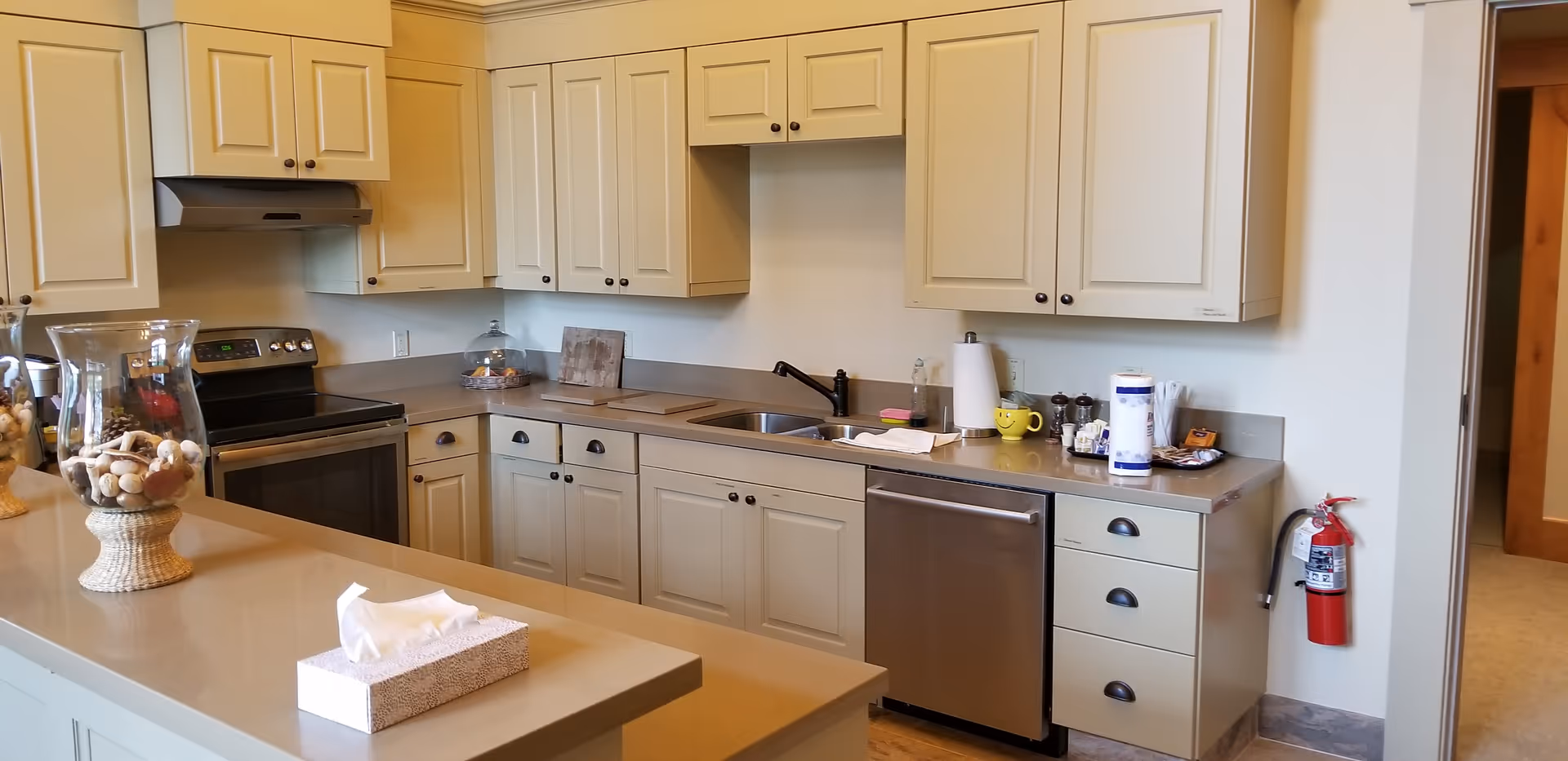 Interior kitchen in a senior living facility with beige cabinets, stainless appliances, and island.