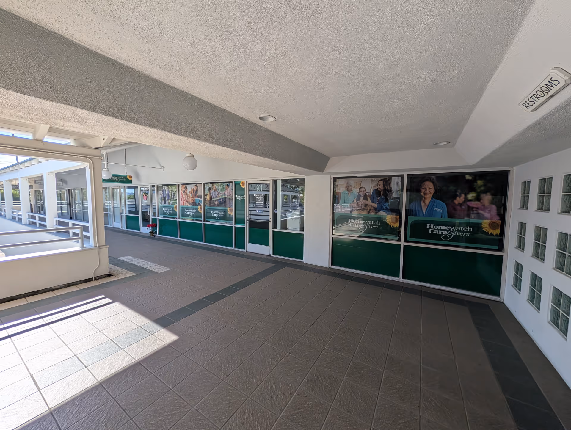 Covered outdoor corridor with windowed storefront ads for Homewatch CareGivers.