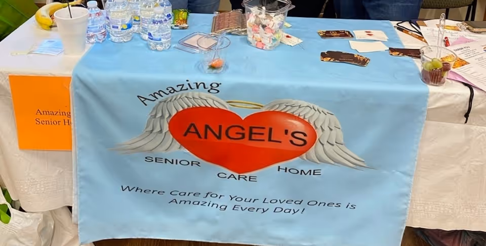 Blue banner with angel wings and heart reading Amazing ANGEL'S Senior Care Home on a table.