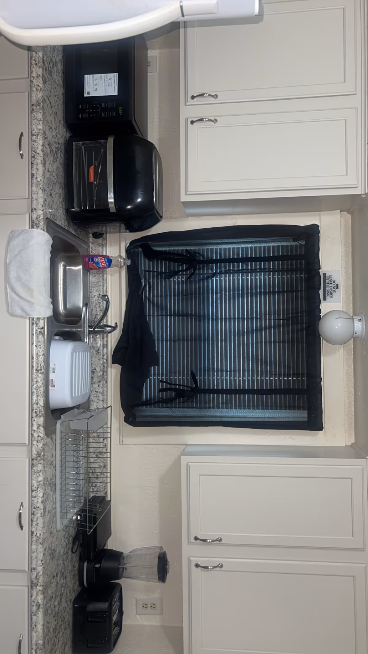 Compact kitchen with sink, appliances, and a window with blinds.