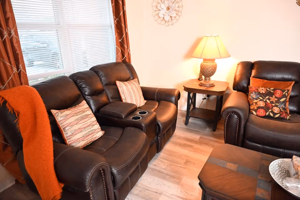 Cozy living room with leather recliners, a side table lamp, and decorative pillows.