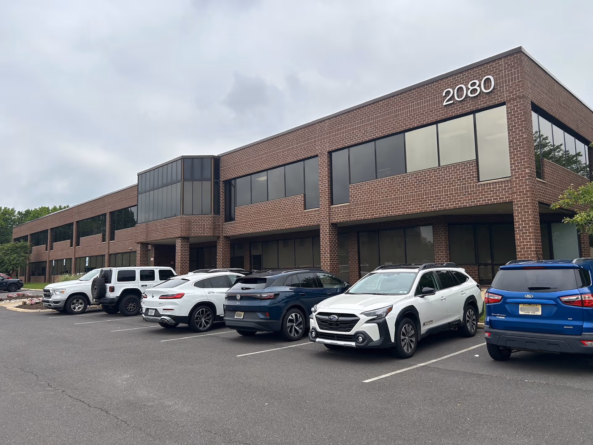 Two-story brick building with large windows and a row of parked cars in front.