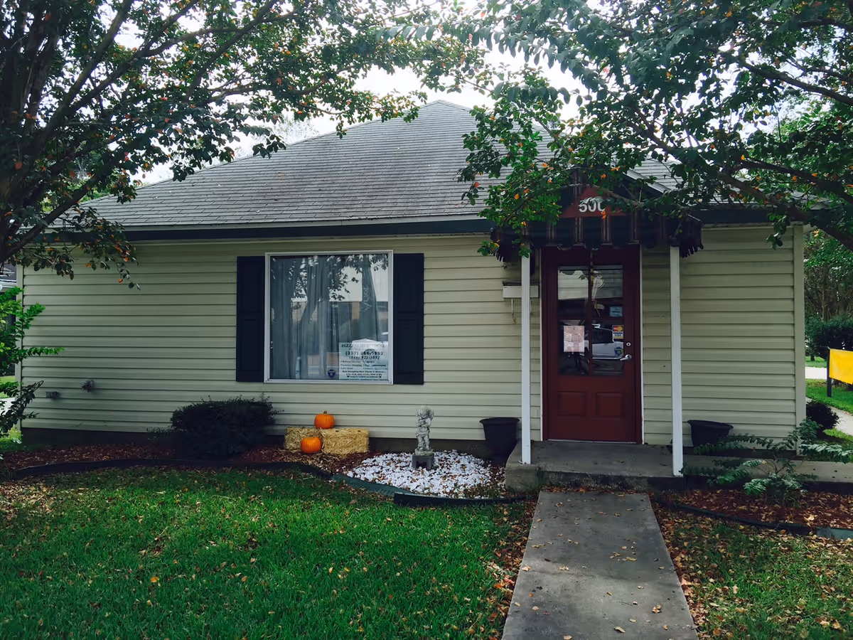 A small beige senior living facility exterior with a red door, pumpkins, and fall decor.