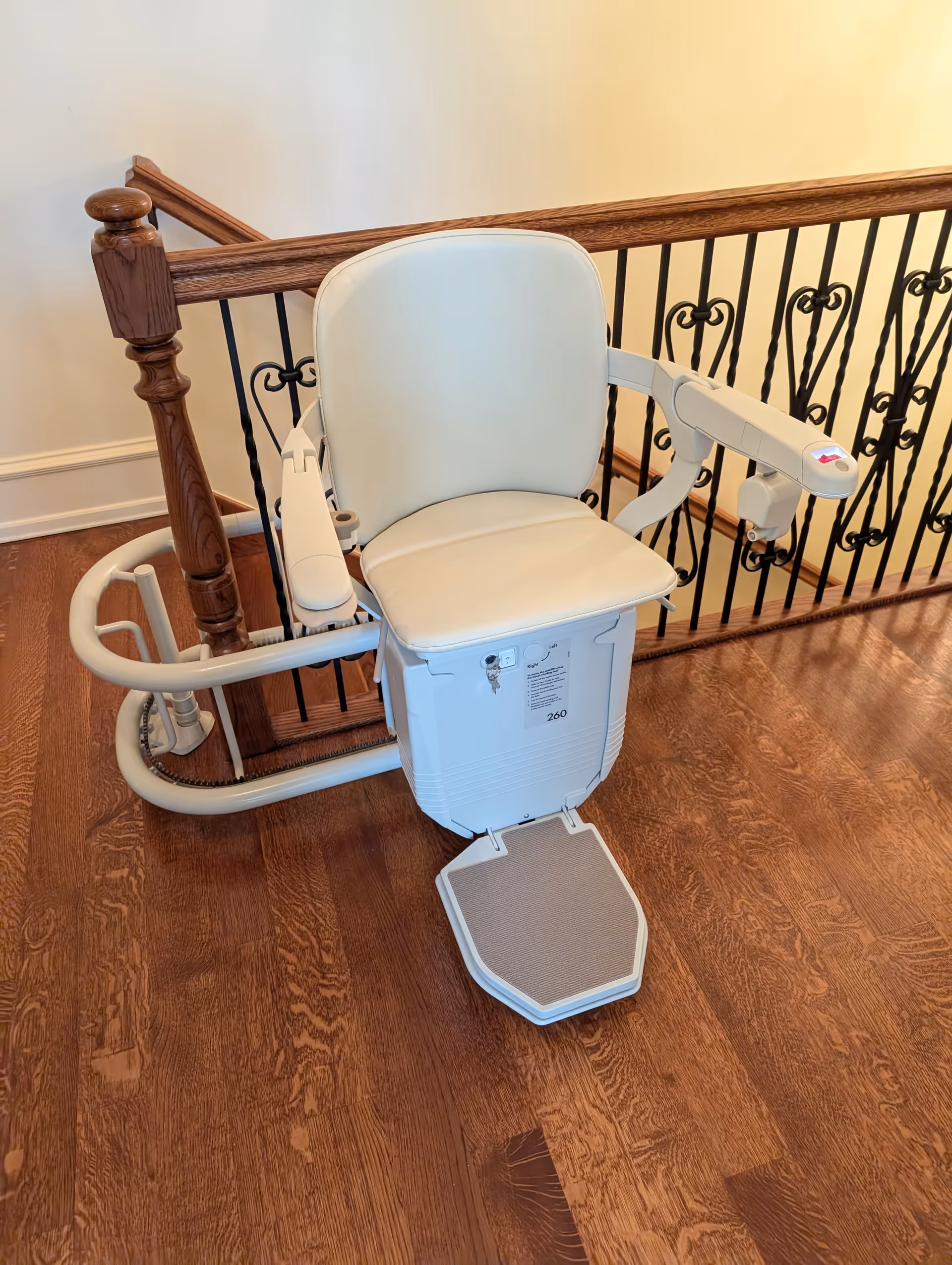 Motorized stair lift with white seat along wooden staircase railing inside a home.