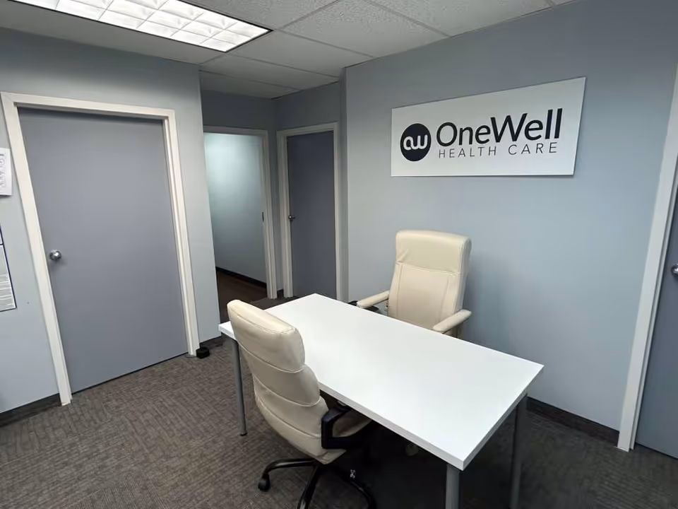 Office reception area with white desk, two cream chairs, and OneWell Health Care sign.