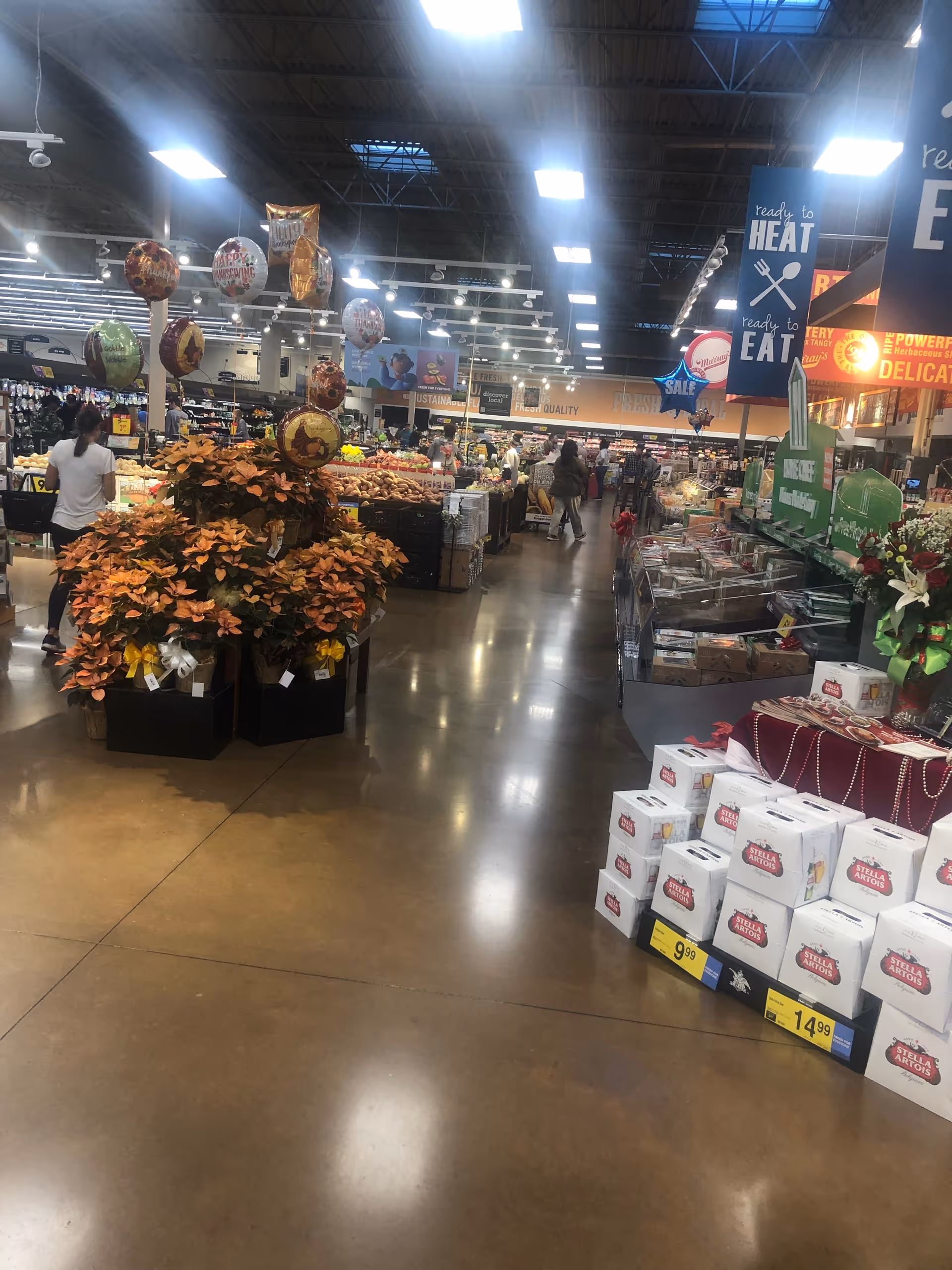 Busy Kroger store interior with produce displays, balloons, and shoppers browsing aisles.