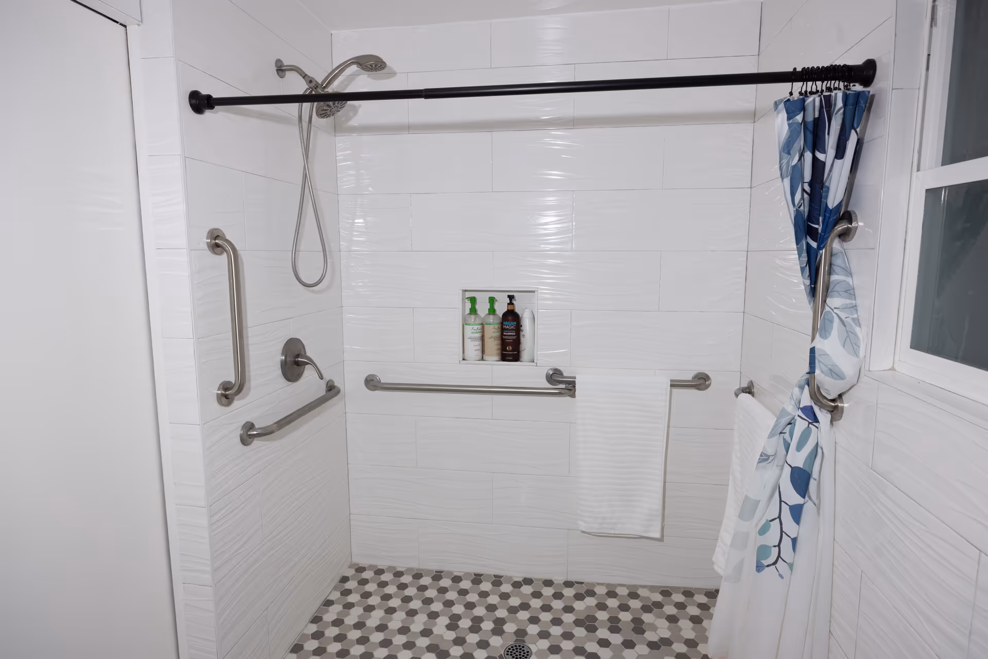Accessible bathroom with a walk-in shower, multiple grab bars, showerhead, and tiled floors.