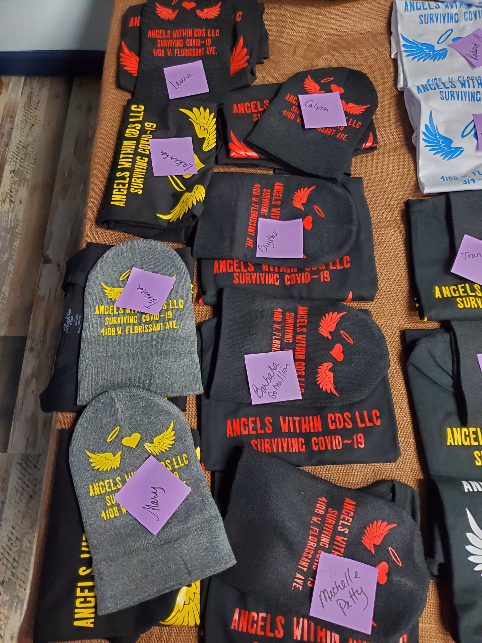 Indoor display of Angels Within CDS LLC COVID-19 gear, with apparel and name tags.