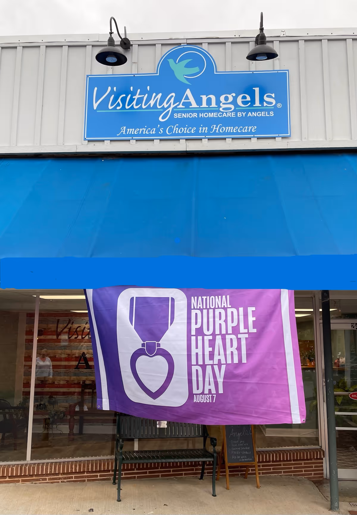 Blue Visiting Angels storefront sign with purple heart banner outside the facility.