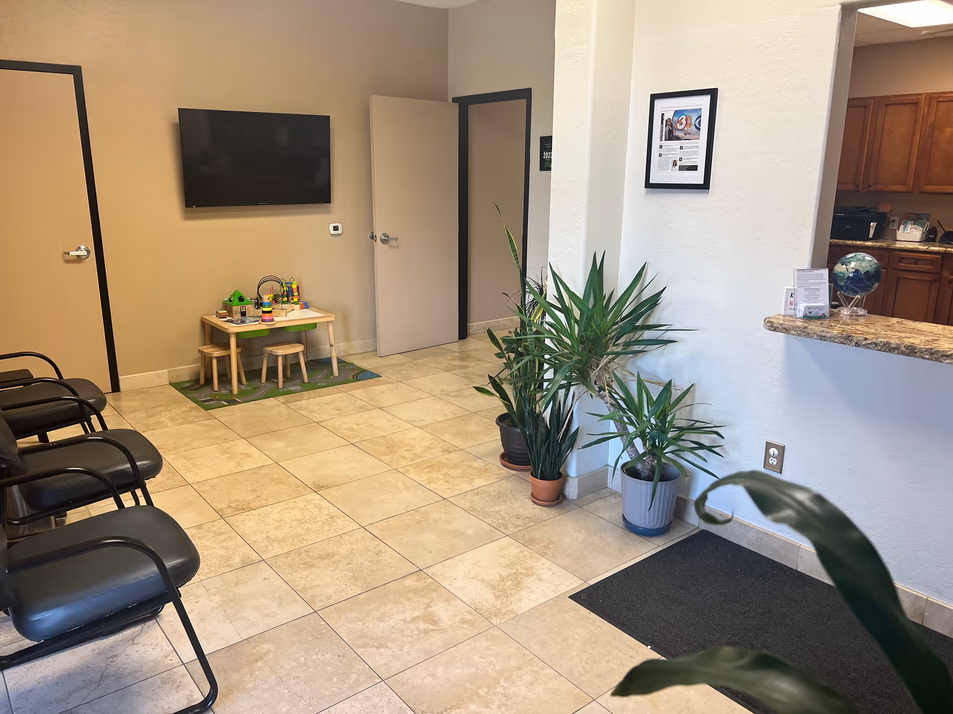 Lobby waiting area with chairs, a small children's table, plants, and a counter.