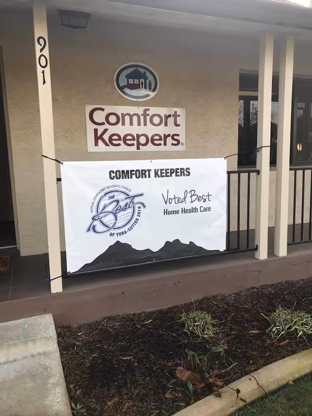 The front exterior of Comfort Keepers Home Care shows banners and the logo.