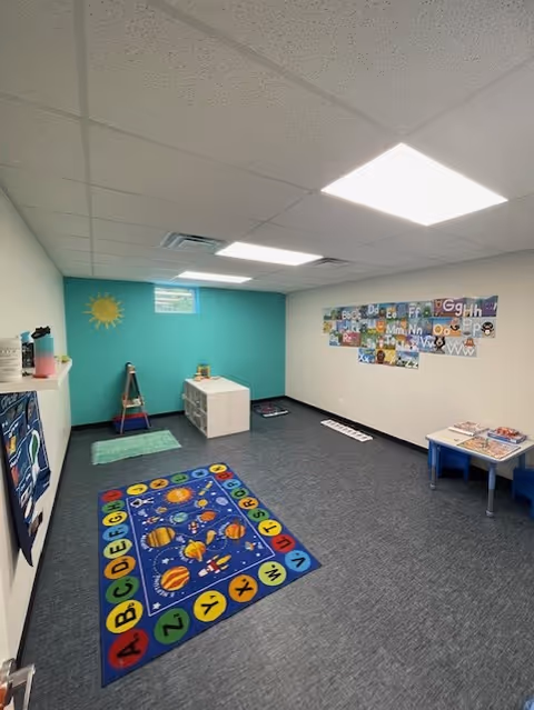 Colorful children's therapy room with alphabet wall, rug, and small tables.