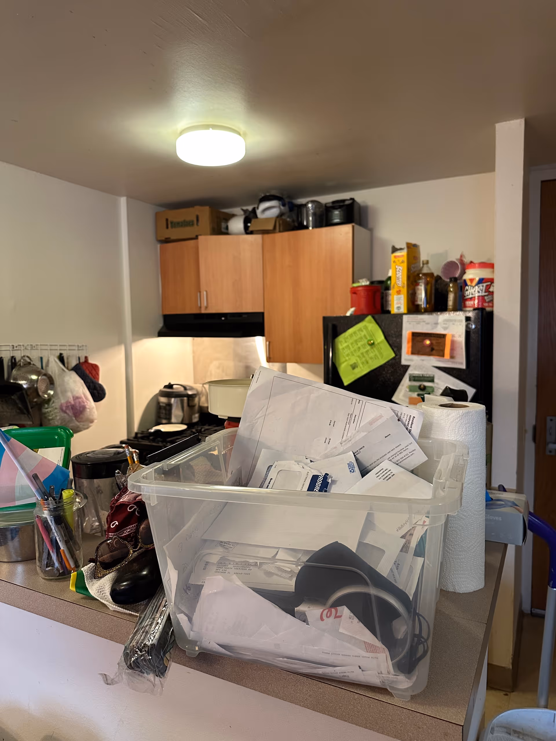 Cluttered kitchen counter with papers, containers, and appliances in a residential facility.
