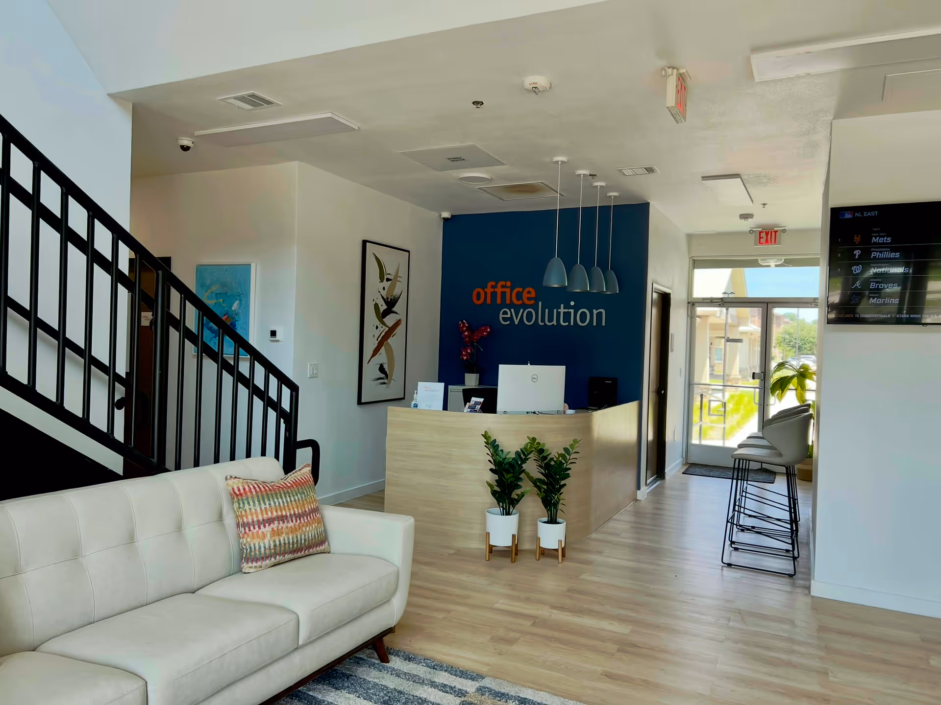Modern facility lobby with white sofa, reception desk, blue accent wall, staircase, and seating.