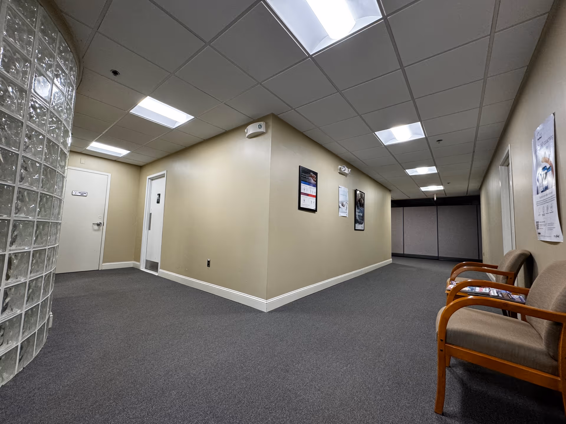 Empty hallway in a senior living facility with beige walls, chairs, and posters.