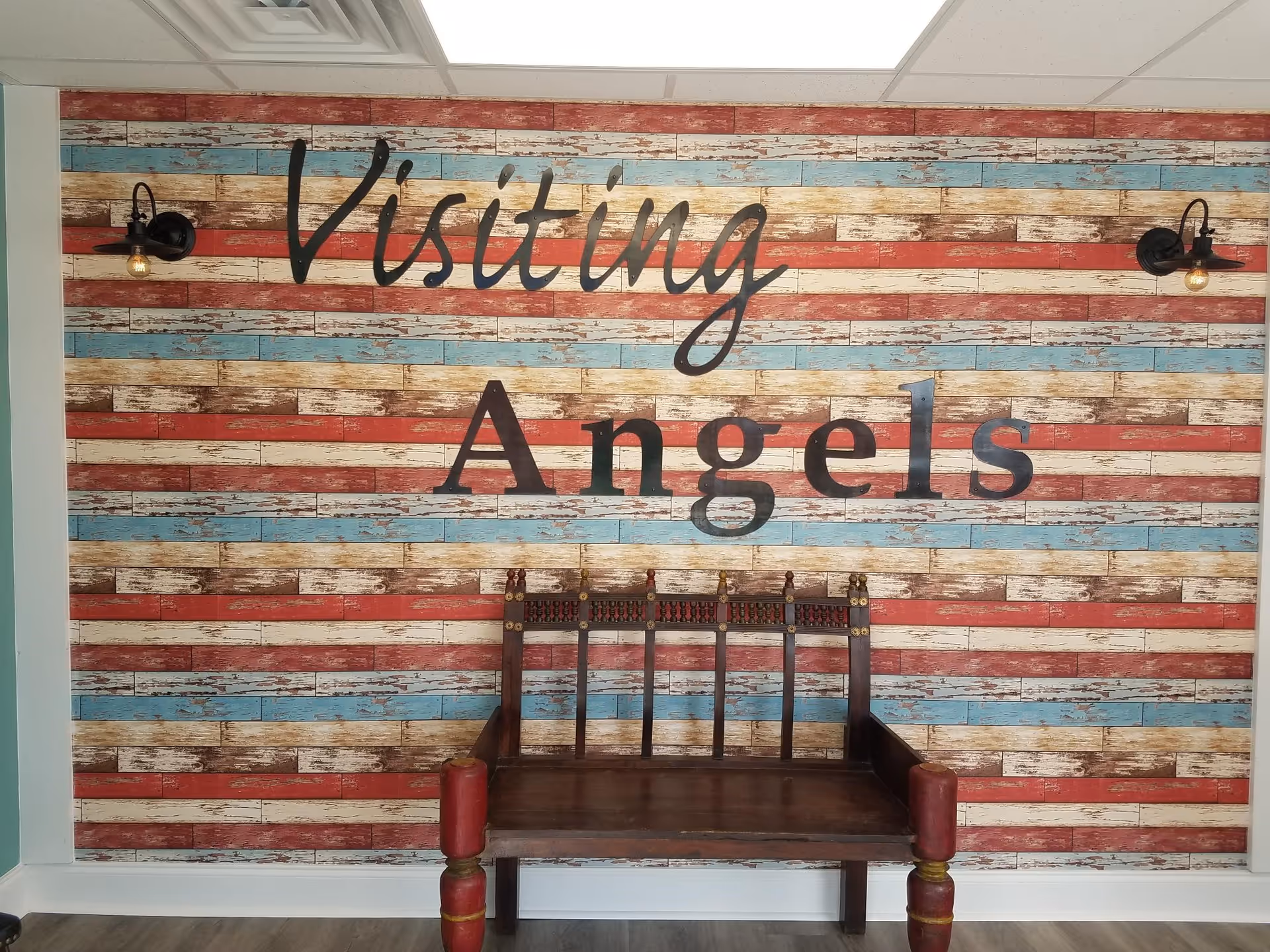 Rustic striped wall with 'Visiting Angels' sign and a wooden bench in a hallway.