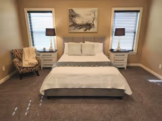 A neatly made bedroom with a central bed, two nightstands, lamps, and an armchair.