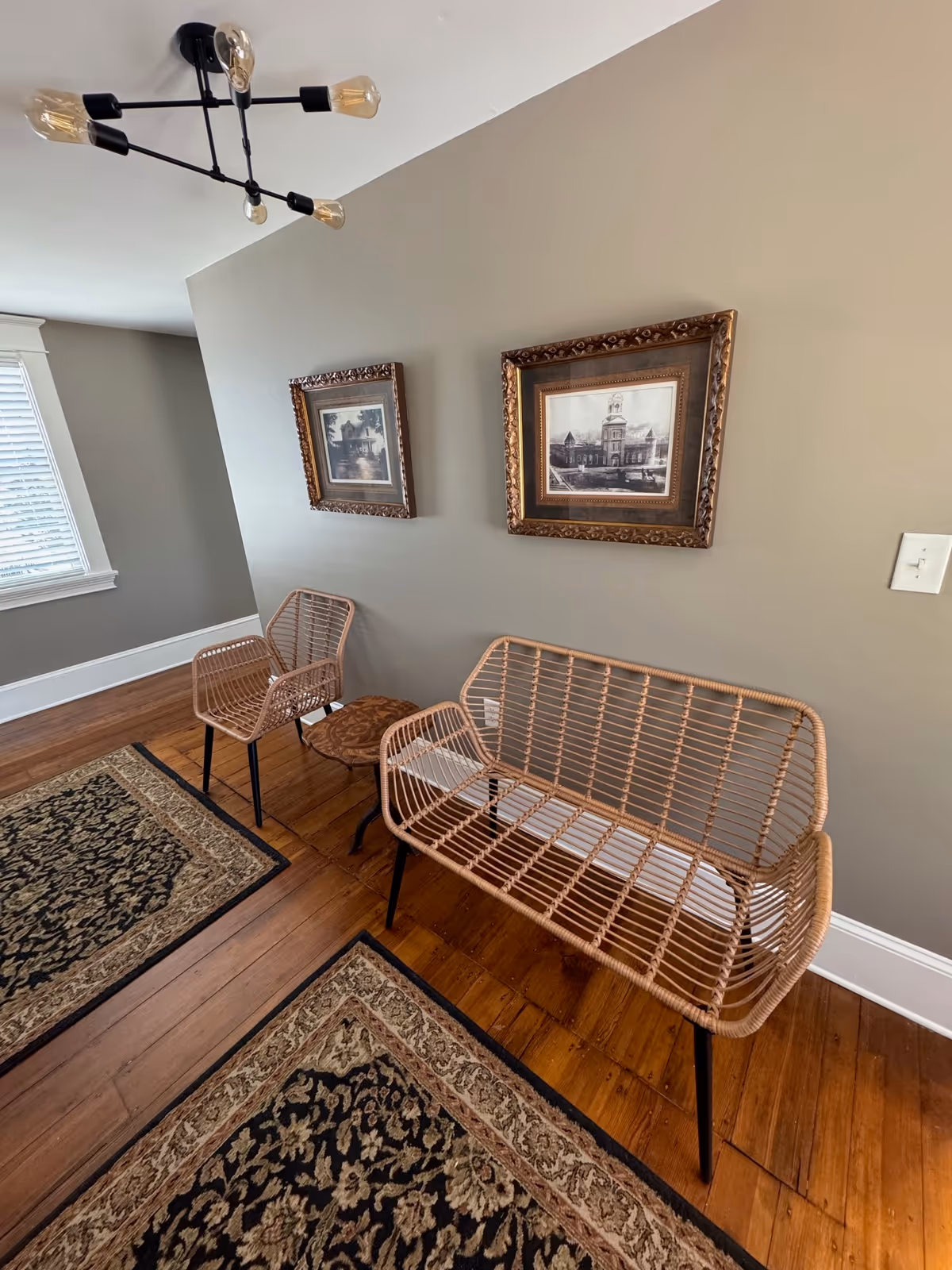 Small waiting area with wicker chairs, framed artwork, and a chandelier on neutral walls.