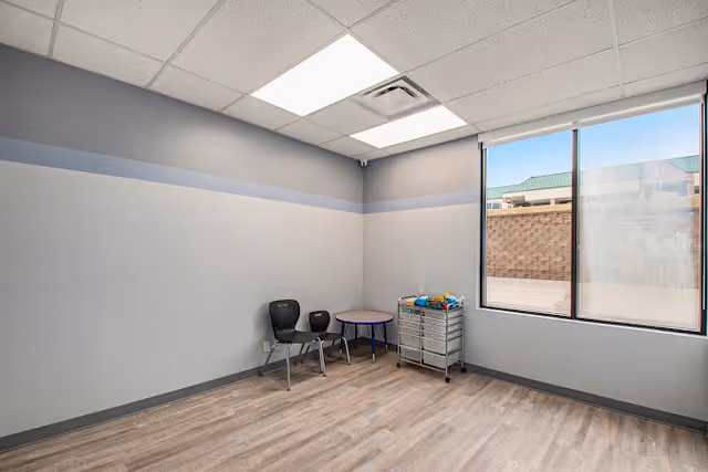 Empty therapy room with two chairs, a small table, and a rolling cart by a window.