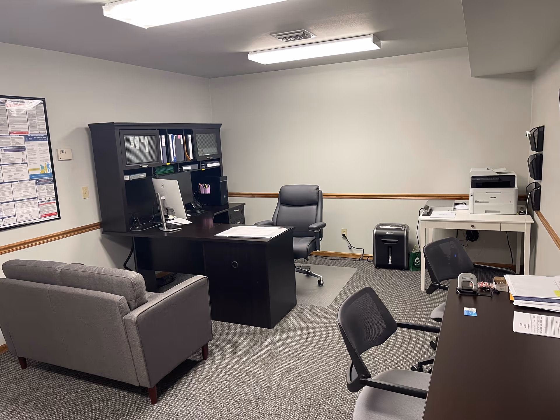 An empty office with desk, chair, couch, printer, and filing cabinet in a small facility workspace.