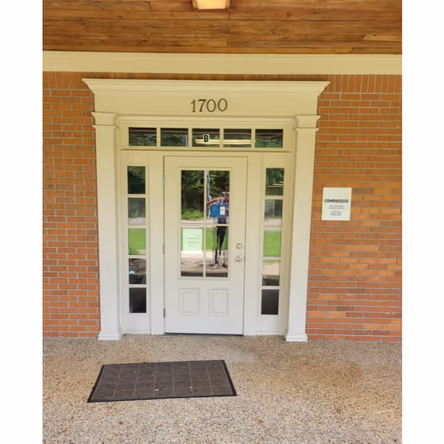 Front entrance of a brick building with white door, address 1700, reflections visible.