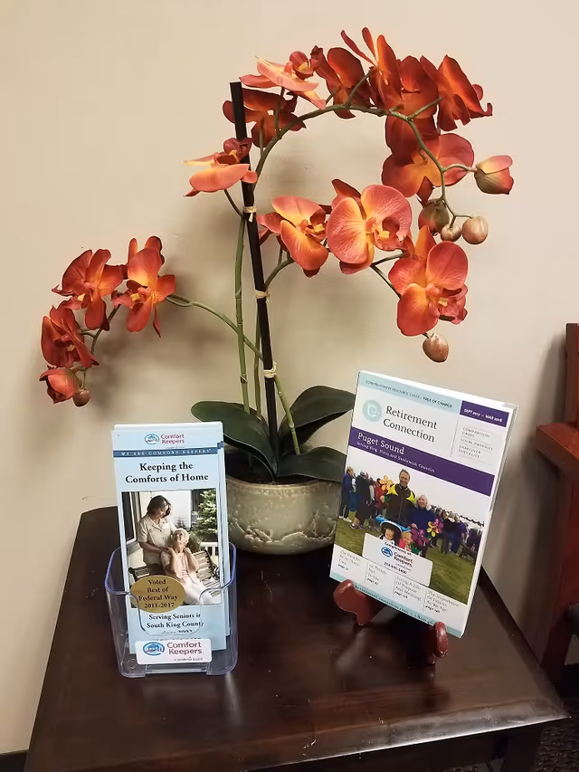 Orange orchid in a pot sits on a wooden table beside facility brochures.