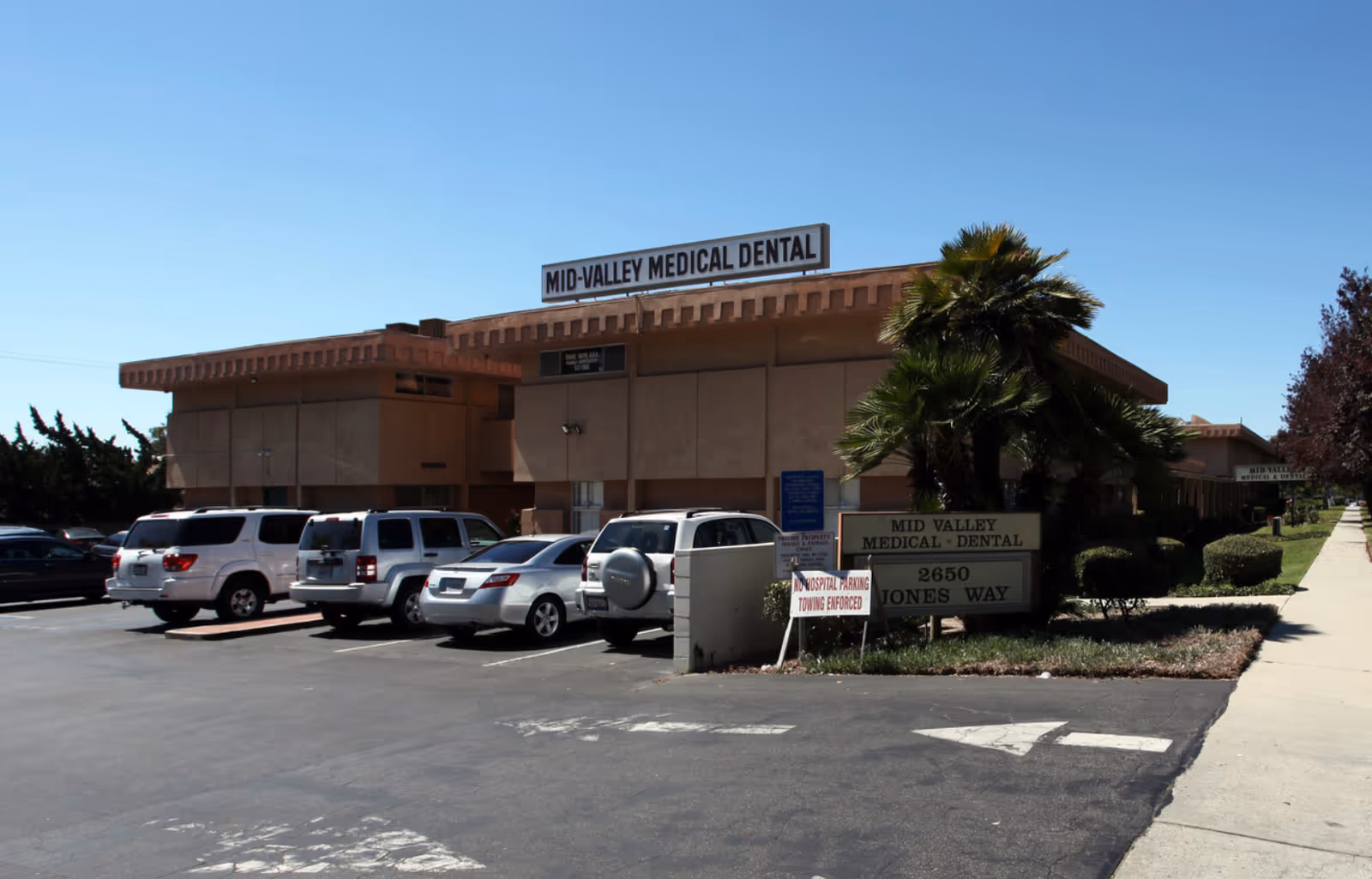 Exterior view of a beige medical-dental building with palm trees and parked cars.