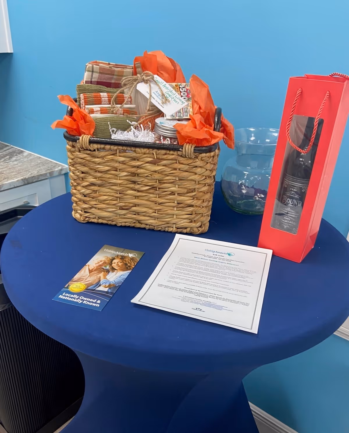 Round blue table with a woven basket, papers, and a pink gift box with wine.