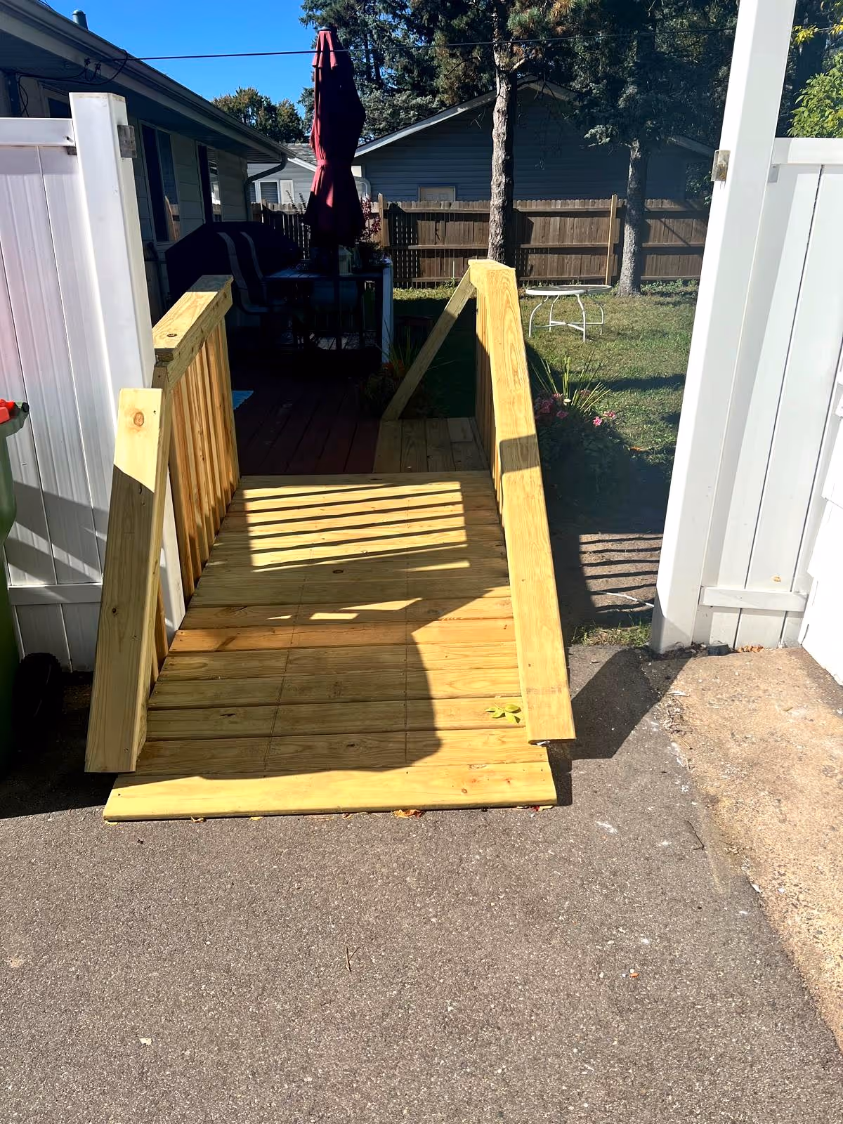 Outdoor wooden ramp leads to a deck with seating in a fenced backyard.