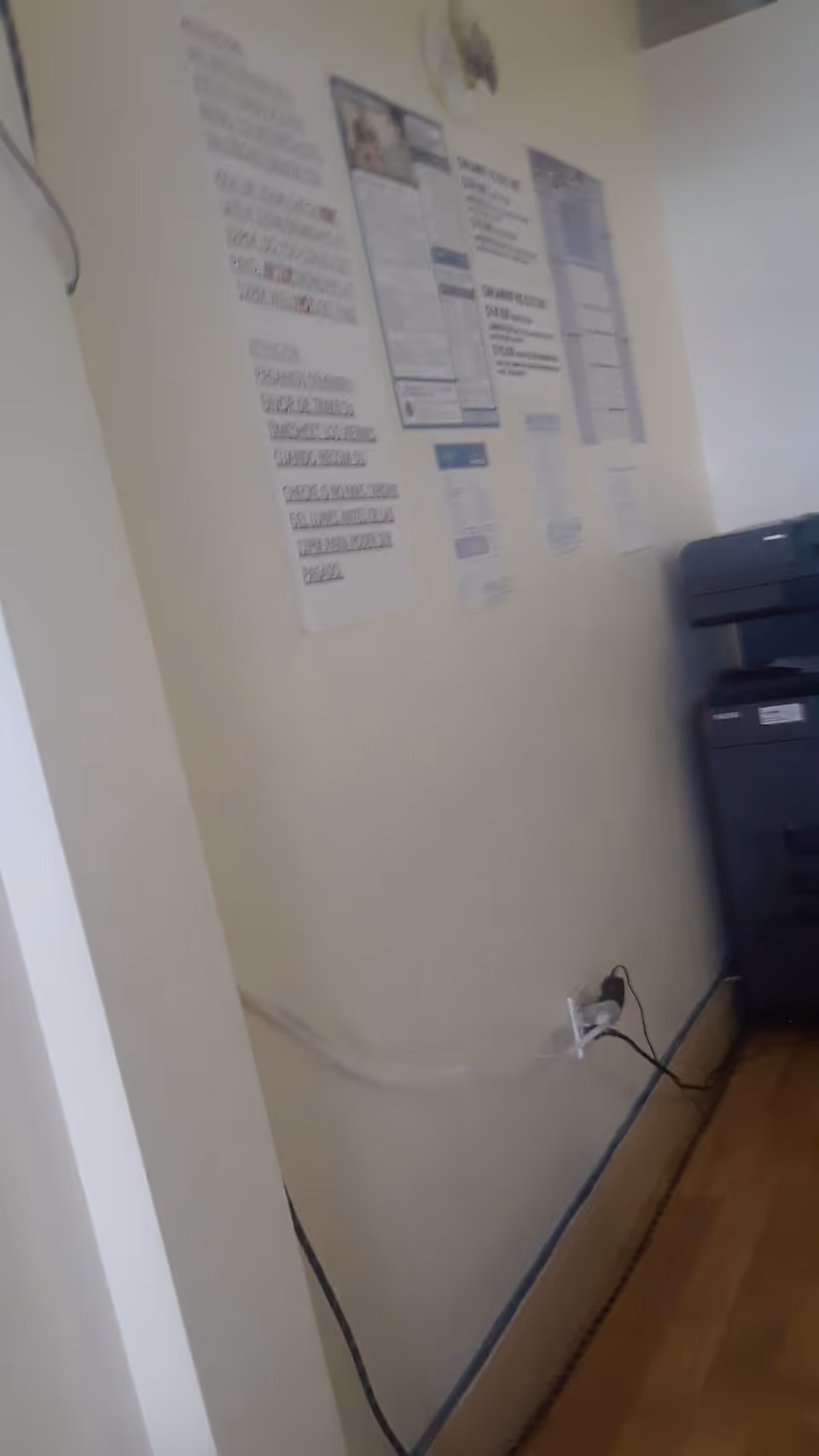 Interior corner of a facility with wall posters, a printer, and exposed cords