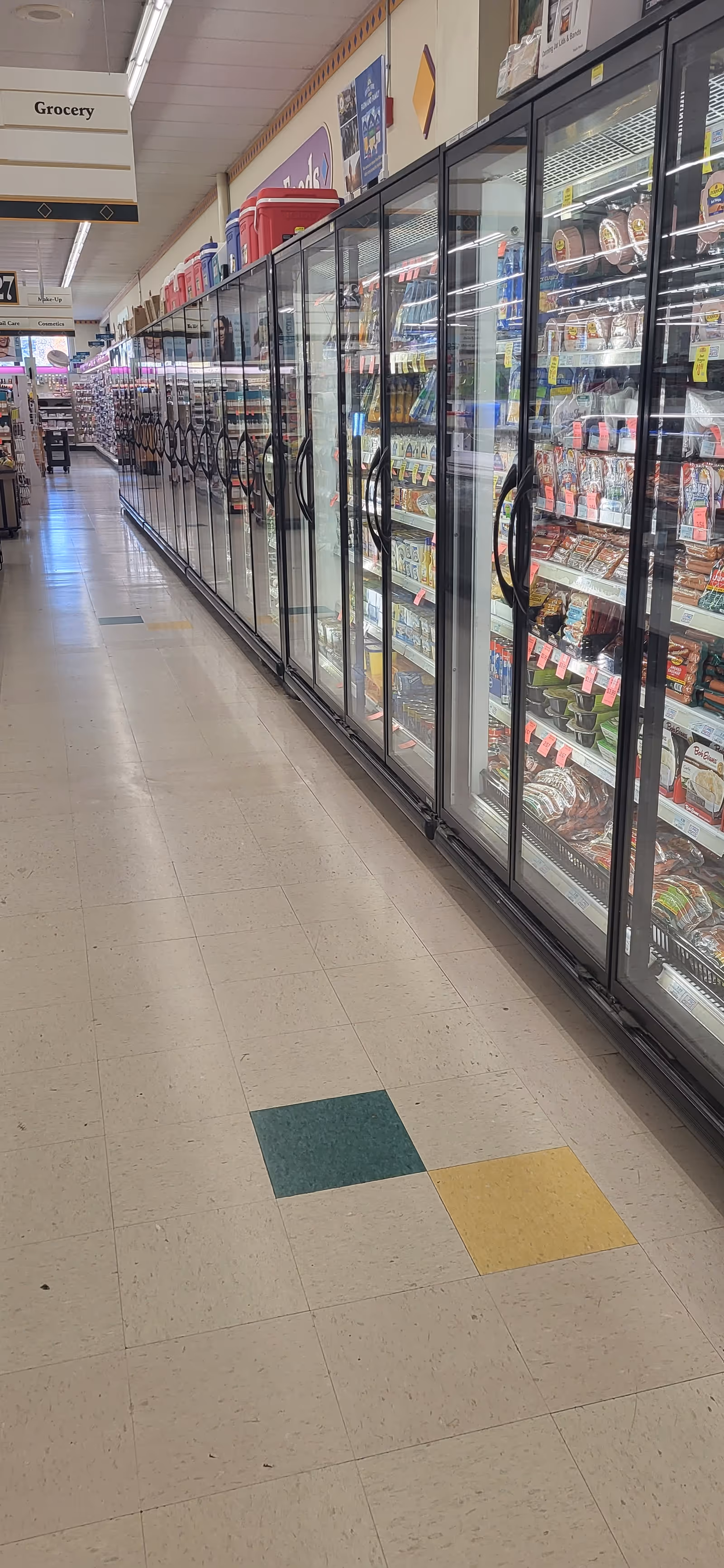 A long grocery store freezer aisle with glass doors and assorted refrigerated products.