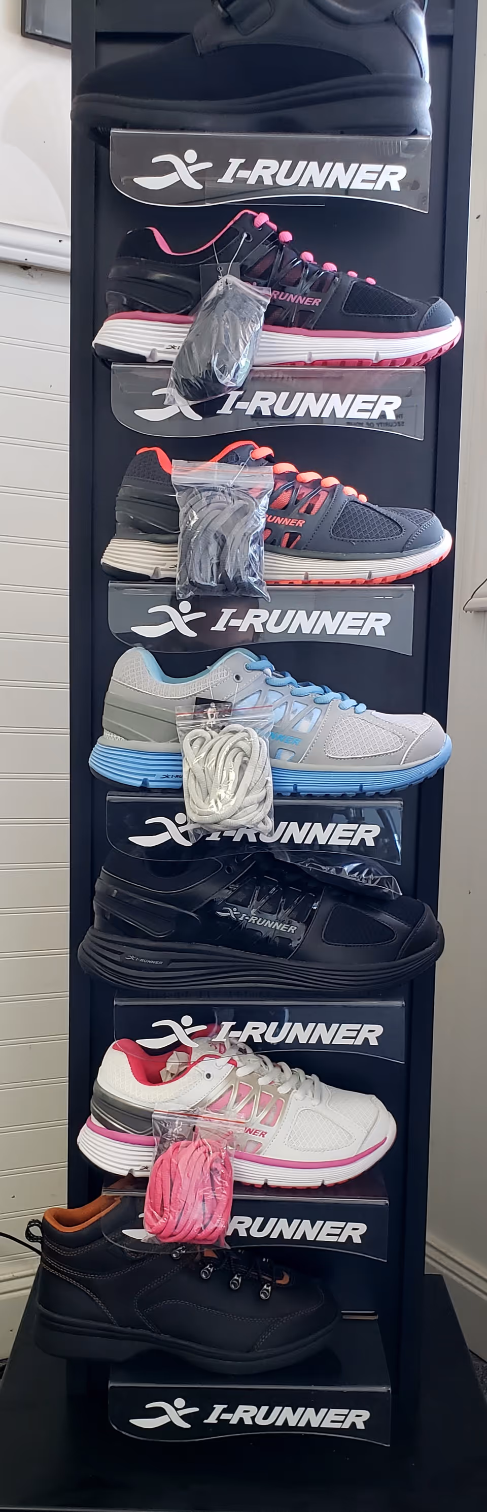 Tall black shoe display rack with multiple I-Runner sneakers inside an interior space.