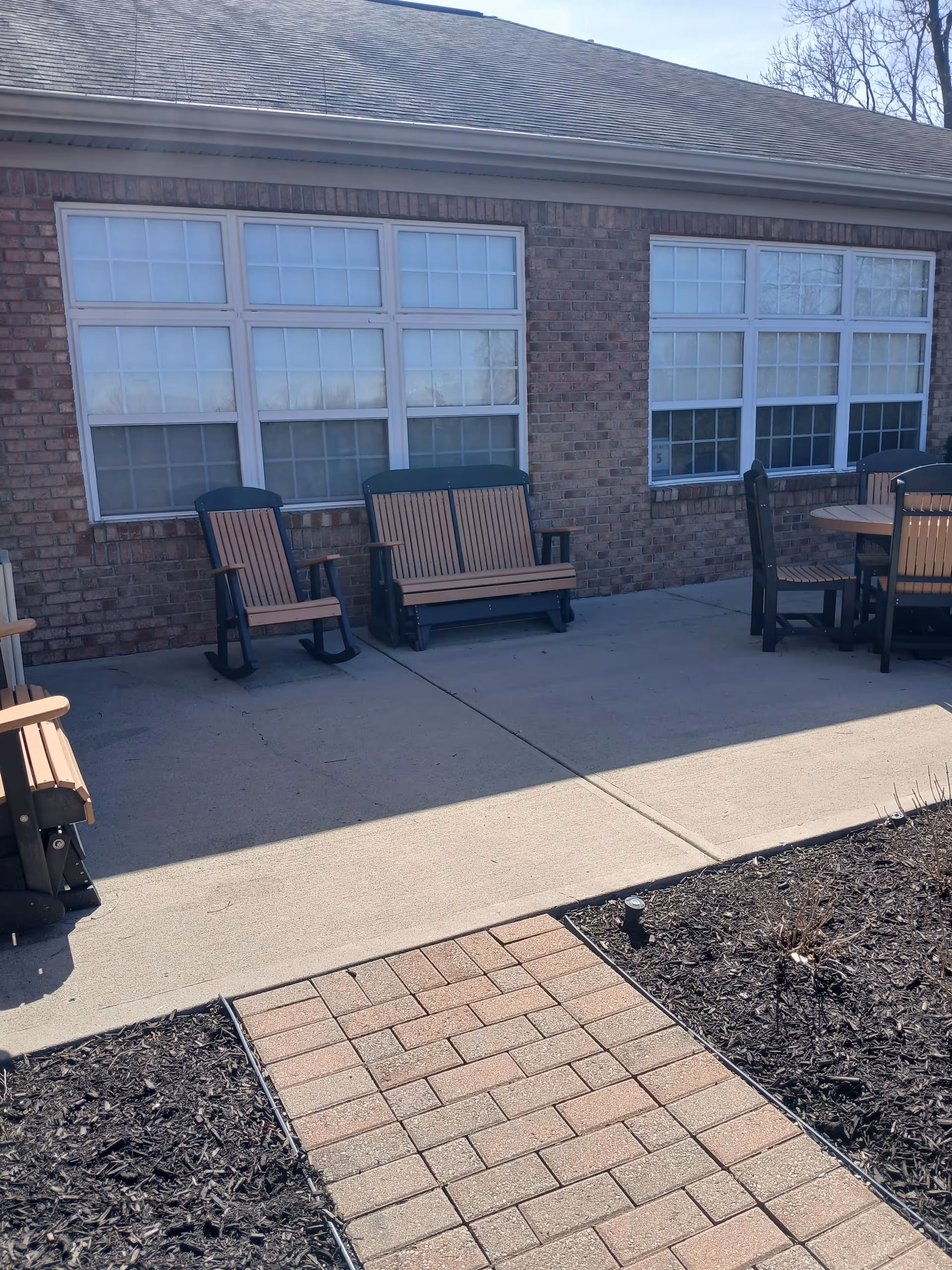 Outdoor seating area along brick building with wooden chairs and tables.